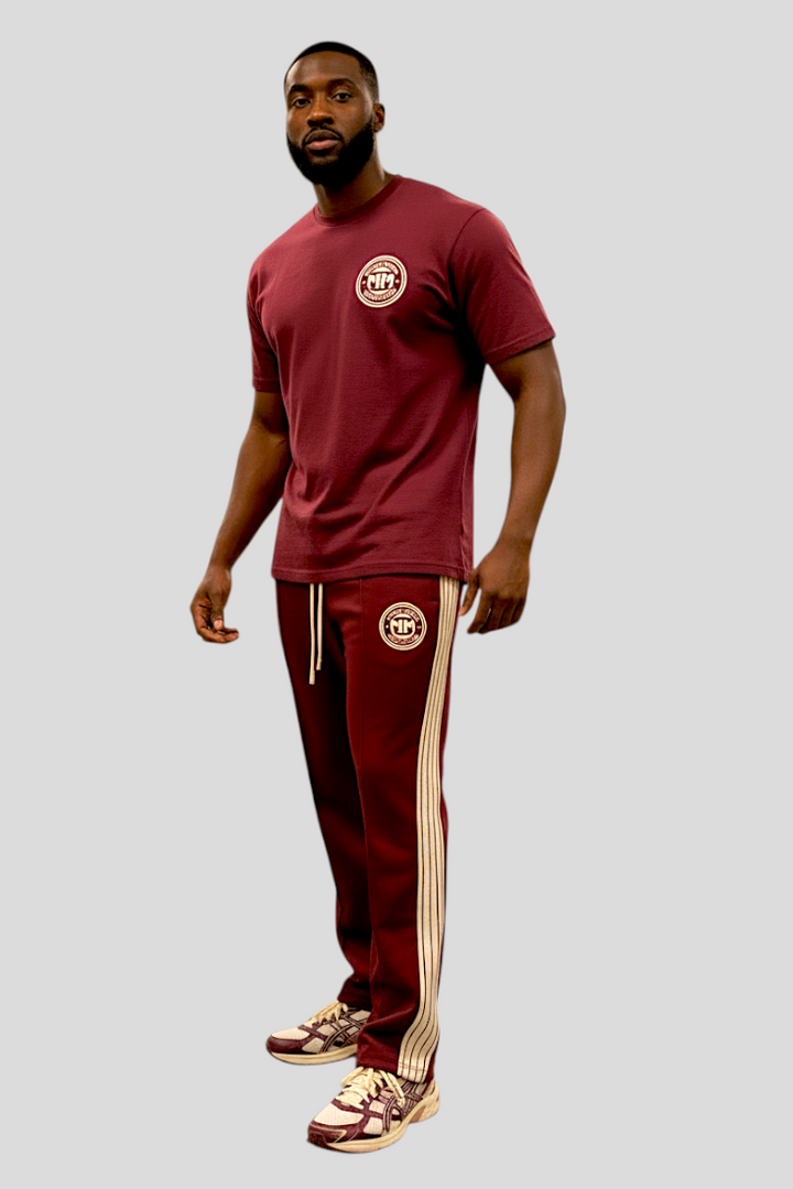 Man wearing maroon UNSTOPPABLE JOGGERS with bold side stripes and matching maroon t-shirt against gray background