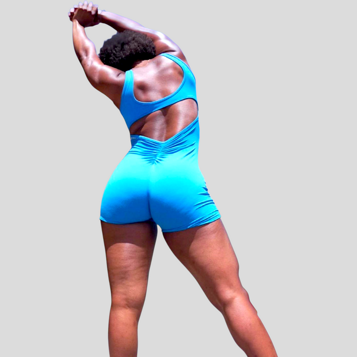 Woman wearing bright blue POWER SLEEVELESS JUMPSUIT 2.0 with V-shaped scrunch back stretching arms