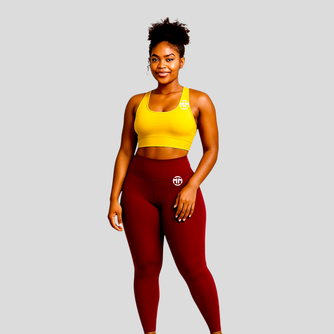 Woman wearing burgundy Power Leggings and yellow sports bra standing against a gray background